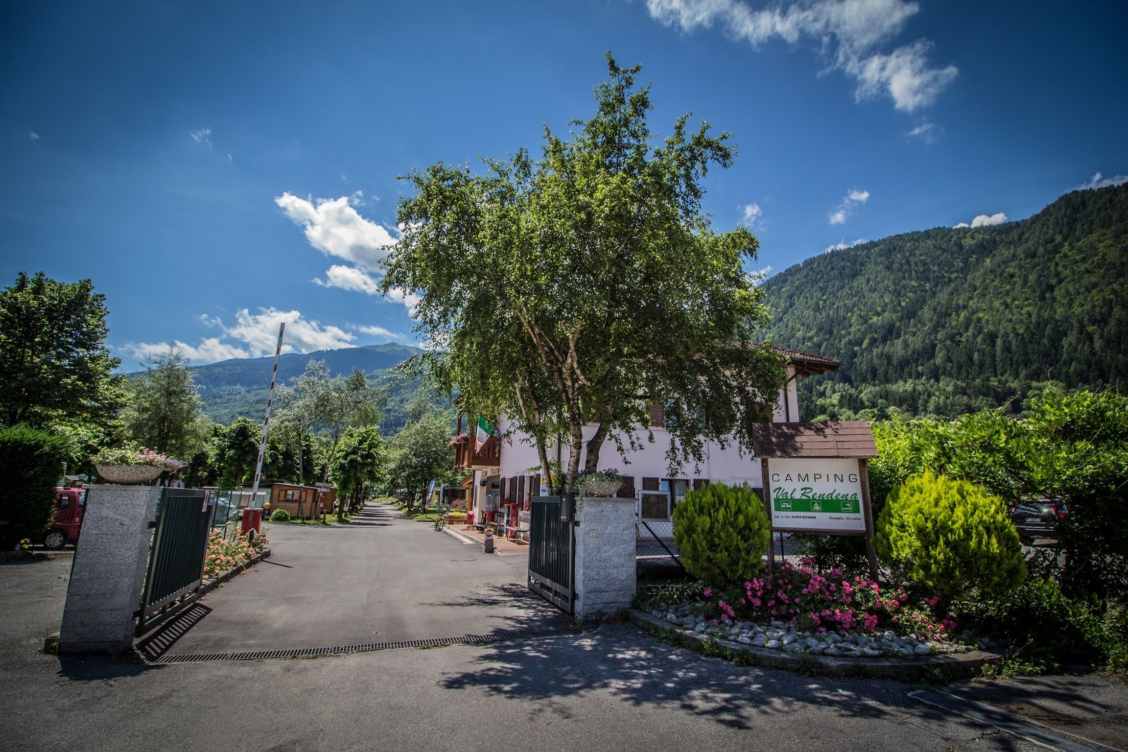 Eingang eines Campingplatzes mit Schild, befestigter Straße und Bergkulisse.