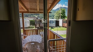 Blick aus einem Zimmer mit Schiebeglastür auf eine Terrasse mit Gartenmöbeln und einen malerischen Berggrund.