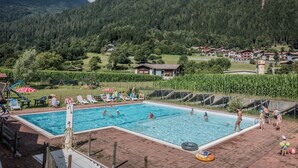 Ein Schwimmbecken, umgeben von üppiger grüner Landschaft, mit Bergen im Hintergrund.