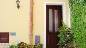 A building entrance with a wooden door, a wall-mounted lamp, and potted plants. - La Casa Siciliana (Custonaci)