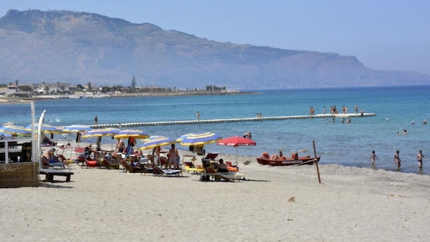 A beach with sun loungers and umbrellas, a pier extending into the water, and people swimming. - La Casa Siciliana (Custonaci)