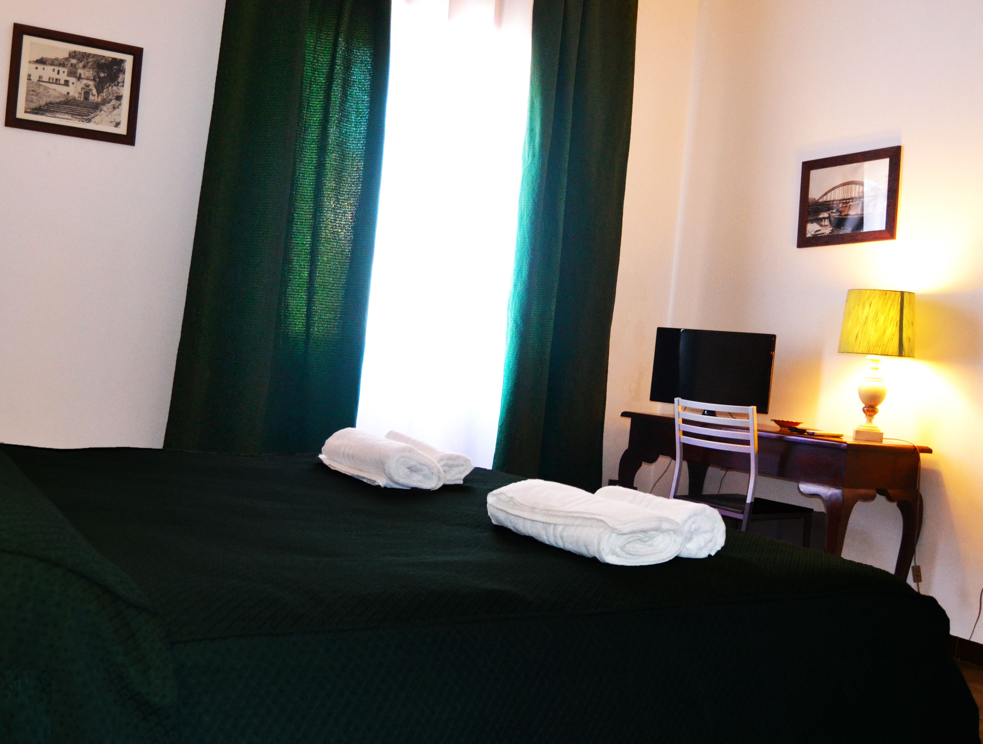 Habitación de hotel con cama, una silla, un escritorio, una lámpara y dos cuadros en la pared.