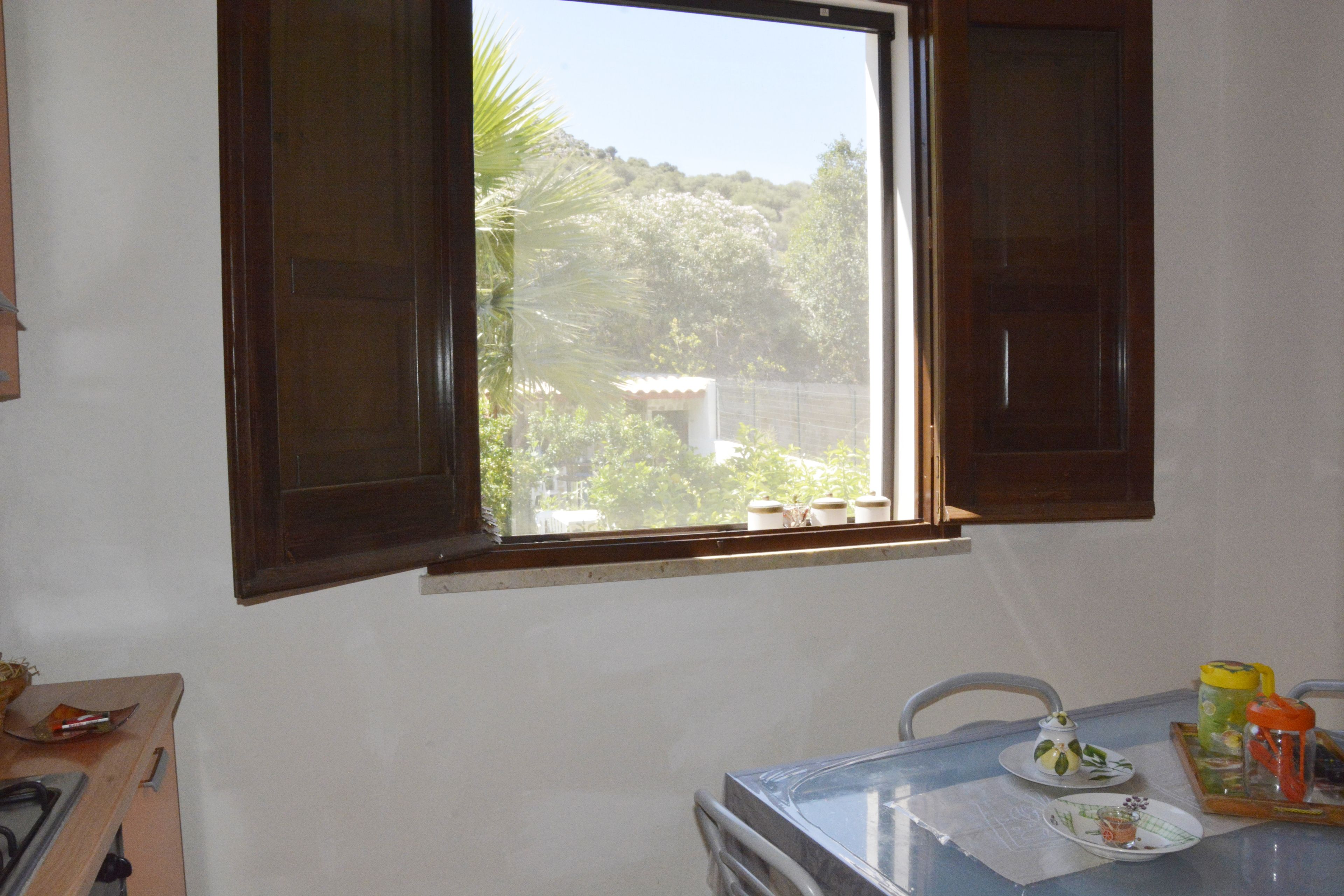 A dining area with a table set for two, a window with curtains, and a view of greenery outside.