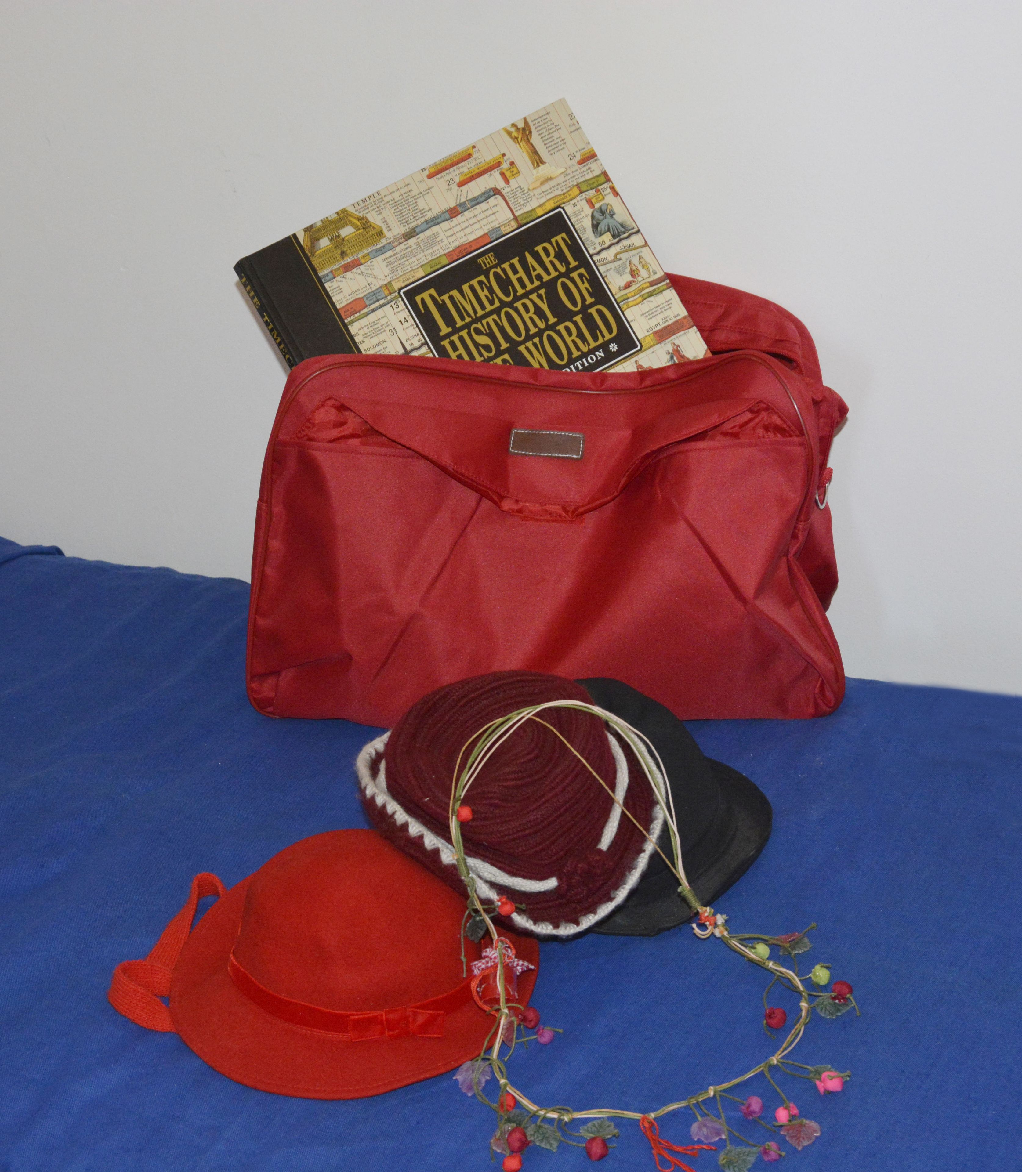 A red bag with a book titled "The Timechart History of World" and two hats on a blue surface.
