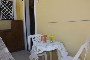 Una pequeña mesa con mantel floral, dos sillas de plástico y dos recipientes encima.