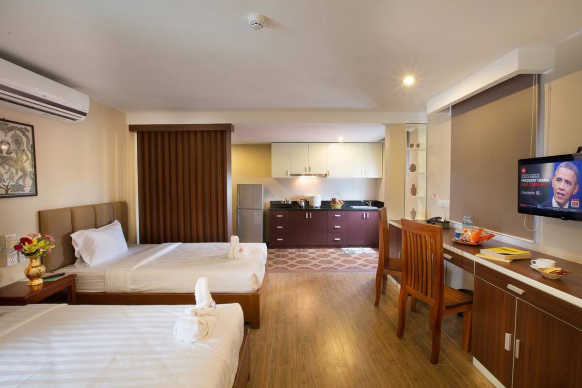 Een hotelkamer met twee bedden, een bureau, een televisie en een kitchenette op de achtergrond.