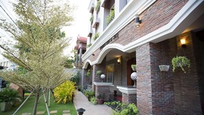 Un hôtel à la façade en briques, doté de nombreux balcons ornés de plantes et d’un jardin bien entretenu avec un sentier.