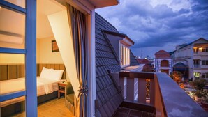 Une chambre d’hôtel avec un lit, une table de chevet et une vue sur le paysage urbain au crépuscule.