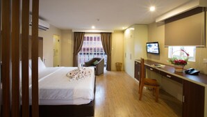 Une chambre d’hôtel avec un lit, un bureau, une chaise, une télévision et une fenêtre avec des rideaux.