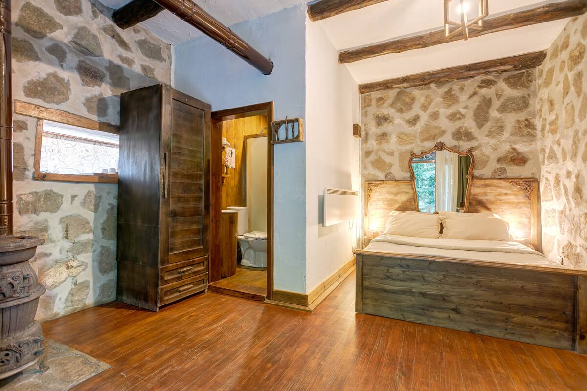 A rustic bedroom with stone walls, a wooden bed frame, and a wooden wardrobe.