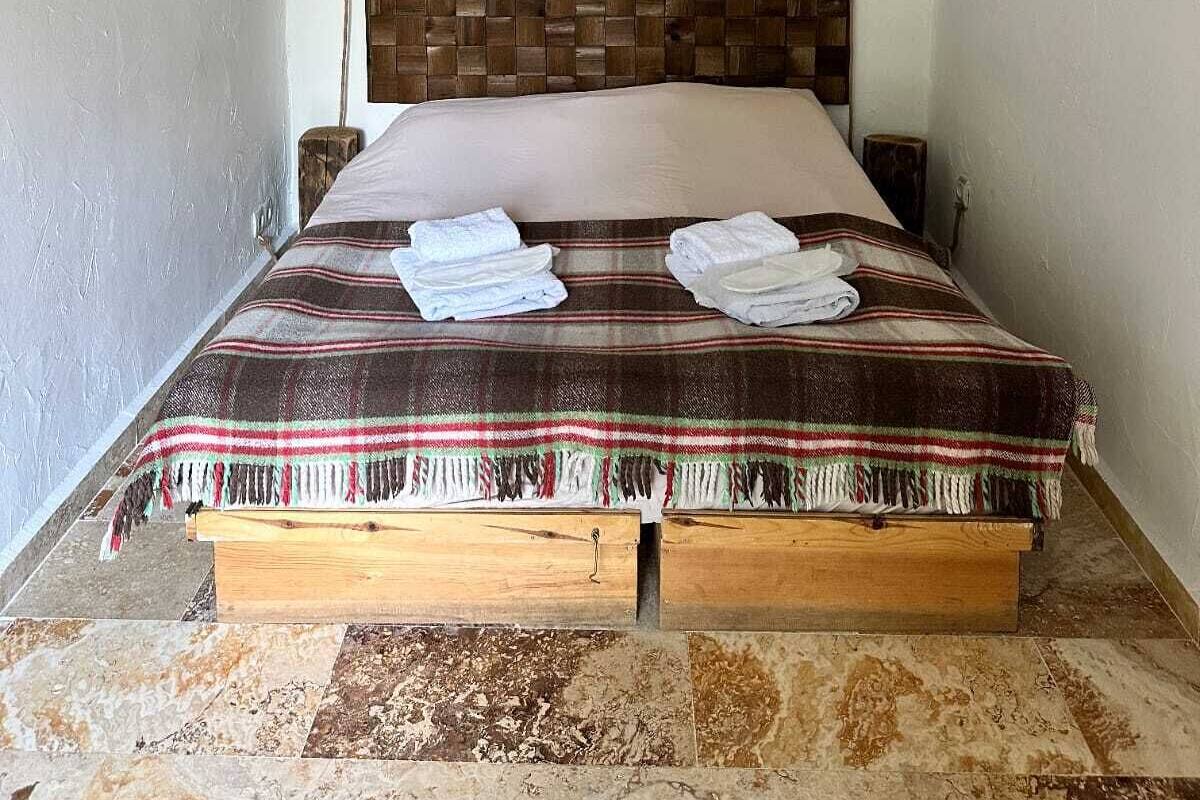 A bed with a wooden headboard, a striped blanket, and two folded towels on the bed.