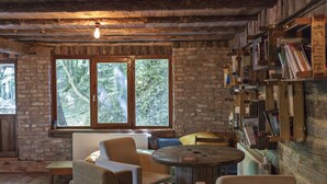 A rustic room with exposed brick walls, a large window with a view of trees, a round wooden table, and a bookshelf filled with books. - Hindiba Doga Evi (Mengen)