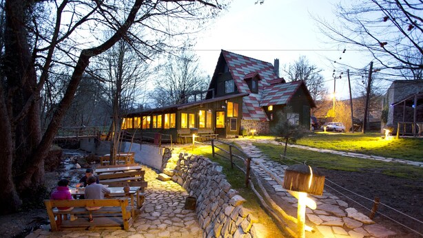 A rustic lodge with stone walls, wooden benches, and a stone pathway leading to a wooden building with a sloped roof. - Hindiba Doga Evi (Mengen)