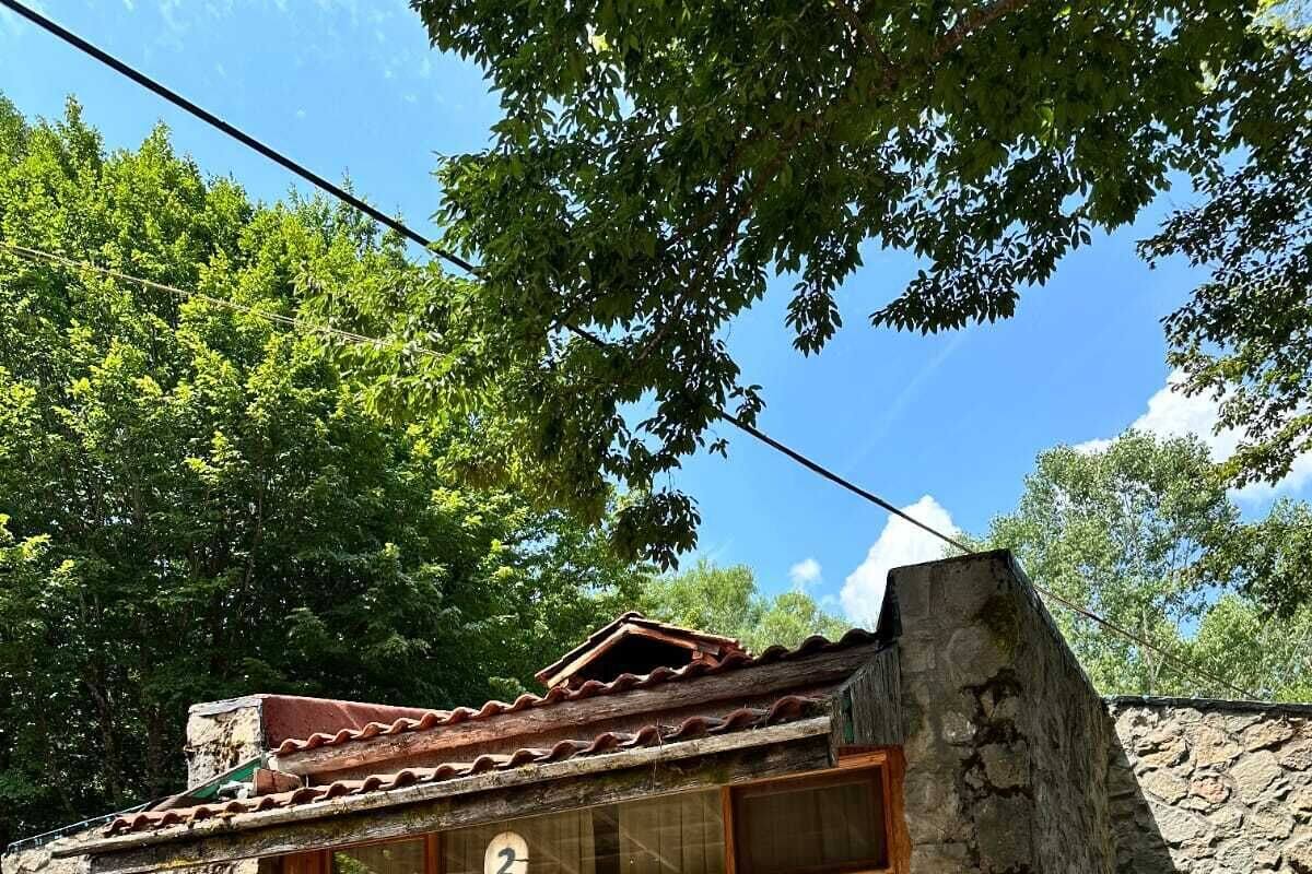 A rustic stone building with a tiled roof, numbered room 2, wooden benches outside, and a stone wall.