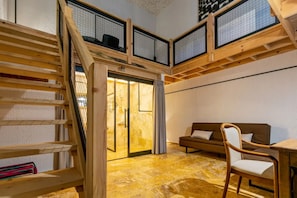 Una habitación con una escalera de madera, un sofá, una silla y un ventanal de vidrio que da a otro espacio.