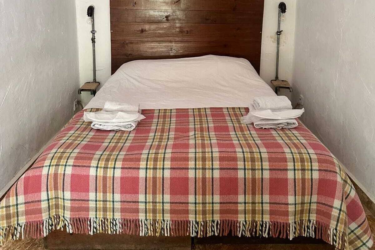 A room with a wooden headboard, a plaid bedspread, and a white wall.