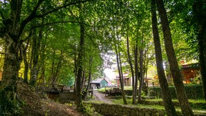 A forested area with a stone bridge, a wooden walkway, and a building with a red roof in the background. - Hindiba Doga Evi (Mengen)