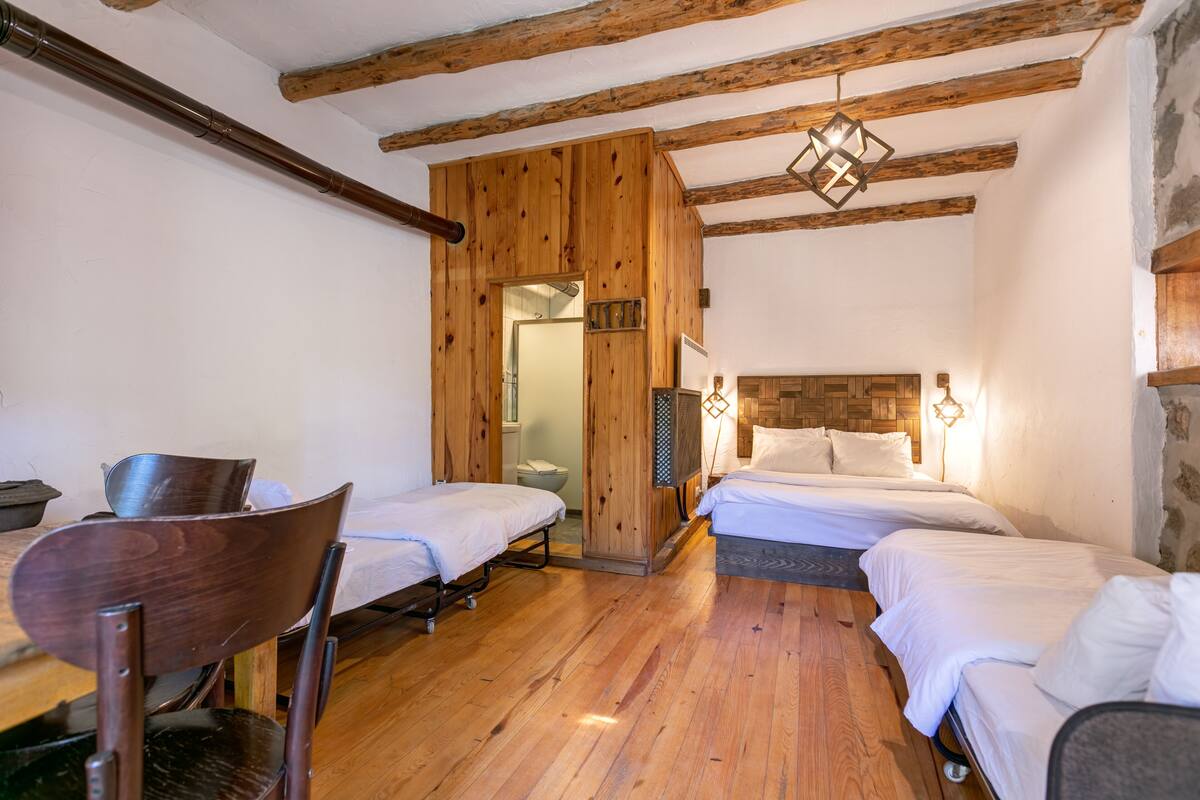 A room with two beds, wooden floors, and a rustic ceiling.