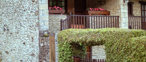 A stone building with a tiled roof, a wooden balcony with flower boxes, and a gate.
