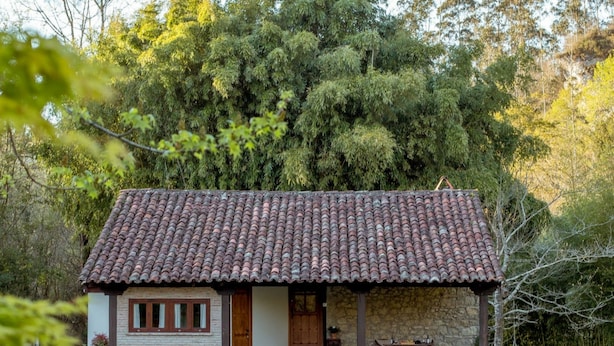 A rustic house with a tiled roof, a stone wall, and a small garden with a pond.