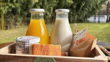 Una caja de madera con frente de malla que exhibe la etiqueta 'EL MOLINO DE BONACO', contiene dos botellas de vidrio con jugo de naranja y leche, un pan y una bolsa de papel con una etiqueta.