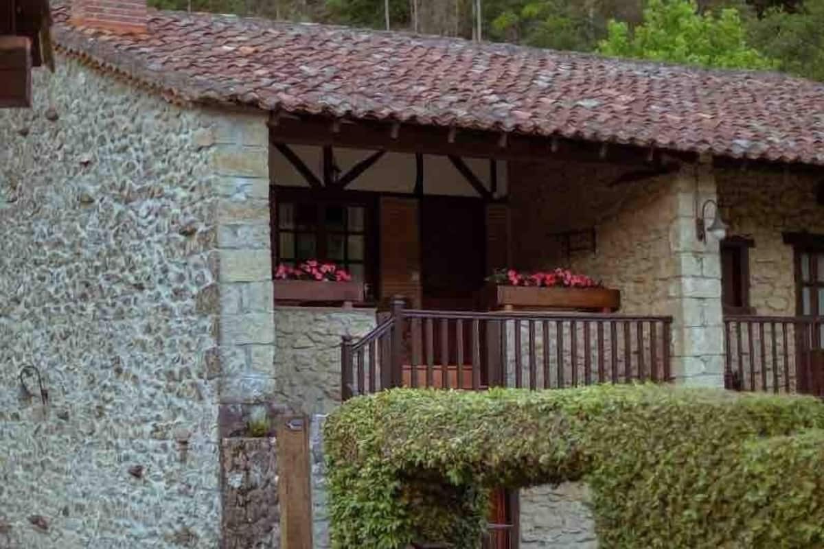 A stone building with a tiled roof, a wooden balcony with a railing, and a gate.