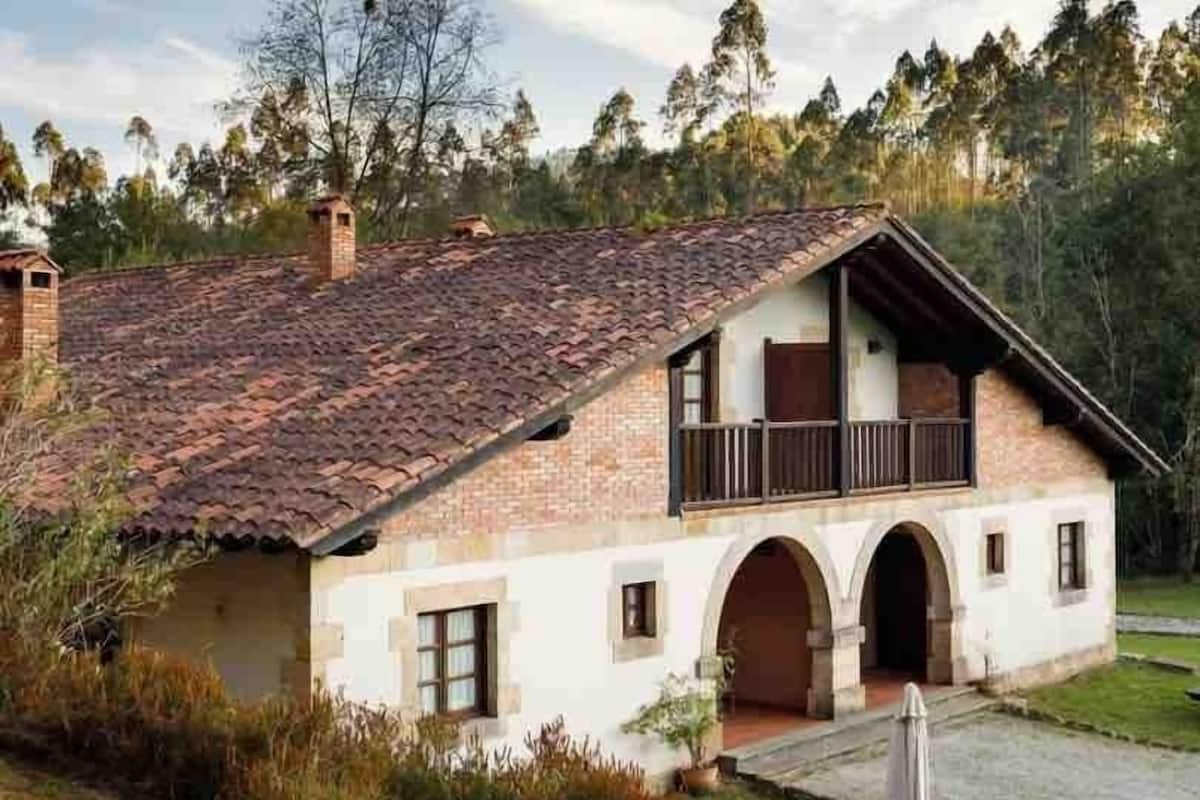 A two-story house with a tiled roof, a balcony, and a stone chimney.