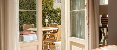 An open door leading to a patio with wicker furniture and a table, a white vase, and a lamp.