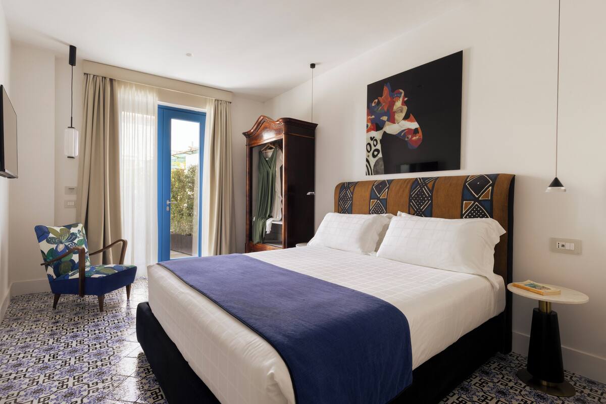 Une chambre d’hôtel avec un grand lit, une chaise, une petite table, une armoire et un tableau au mur.
