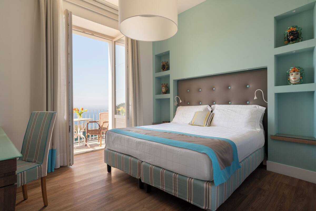 Une chambre dotée d’un grand lit, d’une chaise, d’un balcon avec vue et d’étagères décoratives.