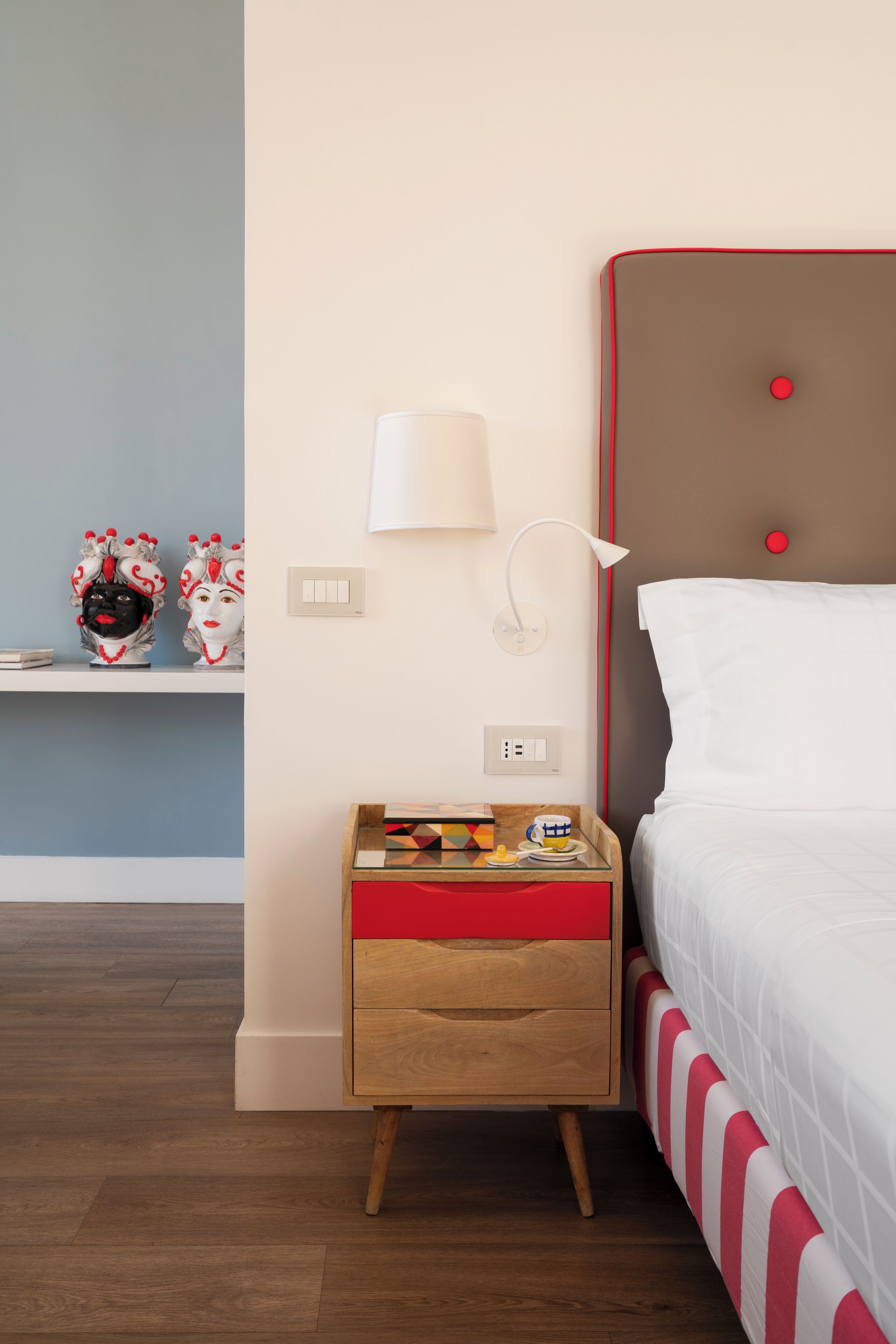 Een verzorgde hotelkamer met een bed, een nachtkastje met een lamp, en een klein plankje met decoratieve objecten.