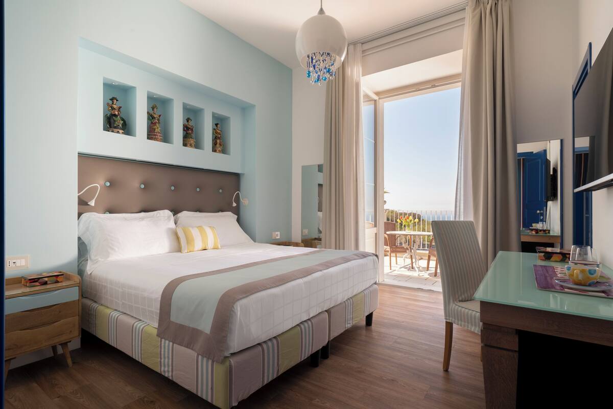 Une chambre d’hôtel dotée d’un grand lit, d’un bureau avec une chaise, d’un balcon offrant une vue et d’éléments décoratifs sur les murs.