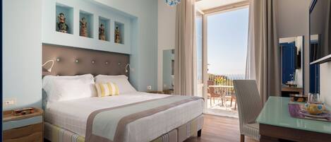 A hotel room with a large bed, a desk with a chair, a balcony with a view, and decorative items on the wall.
