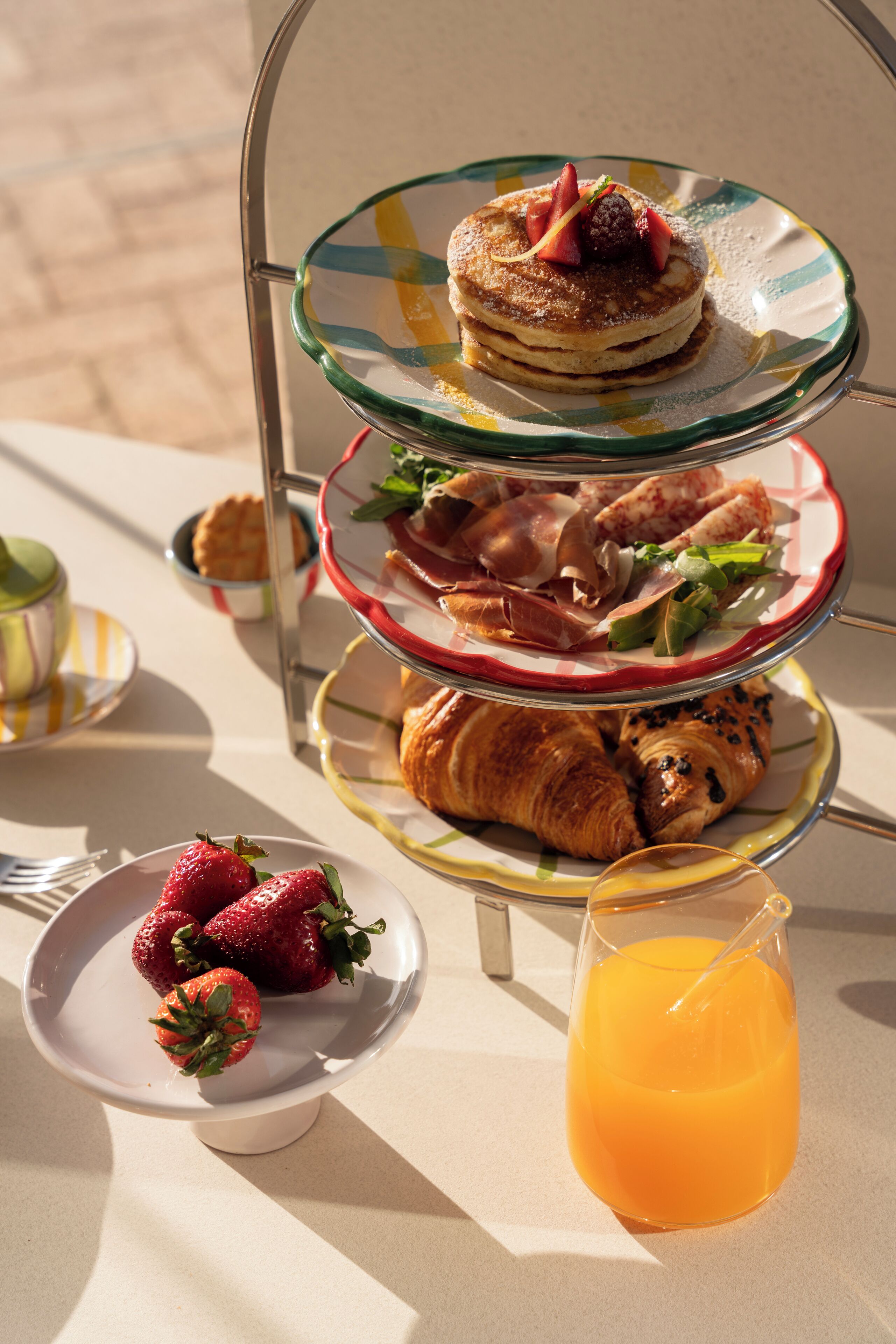 Un plateau à trois niveaux garni de pâtisseries, une assiette de fraises et un verre de jus d’orange.