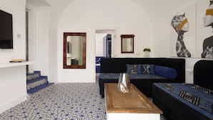 Een woonkamer met een zwarte bank, blauwe kussens met een patroon, een houten salontafel en een grote spiegel aan de muur.