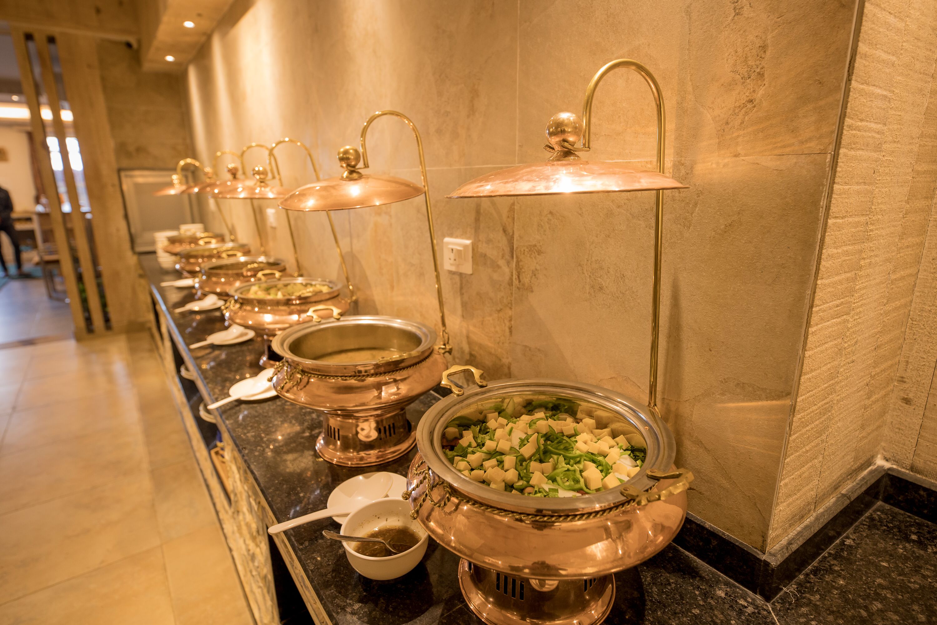 A buffet line with various food stations, including a large pot of diced vegetables and a bowl of soup.