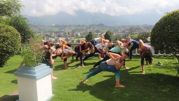 A group of people performing yoga in an outdoor setting with a cityscape in the background.