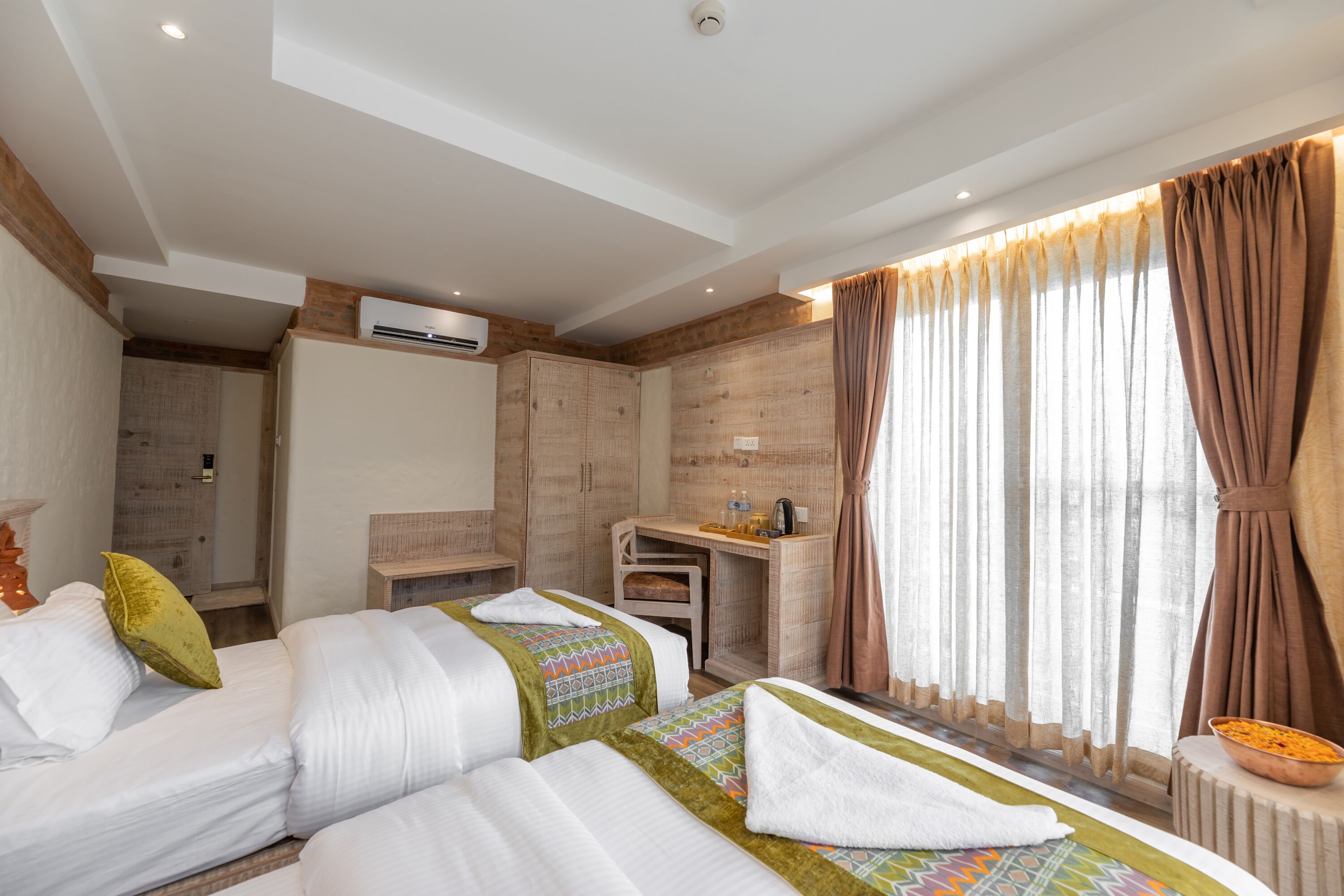 A hotel room with two beds, a desk, a shower area, and a large window with curtains.
