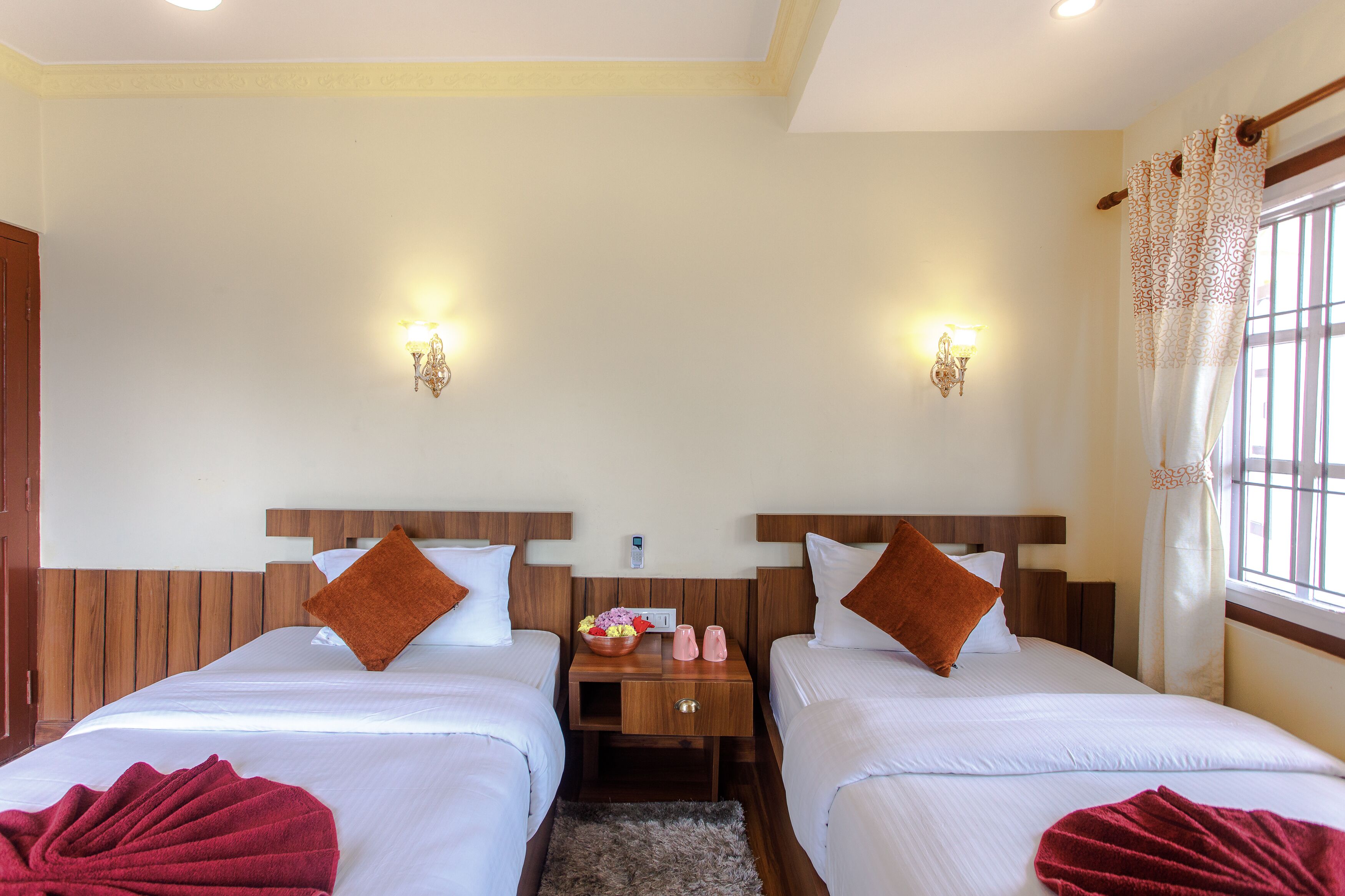 A hotel room with two beds, a nightstand with a lamp, and a window with curtains.