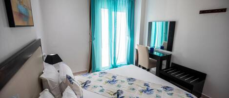 A hotel room with a bed, a desk, a chair, a television, and a window with curtains.