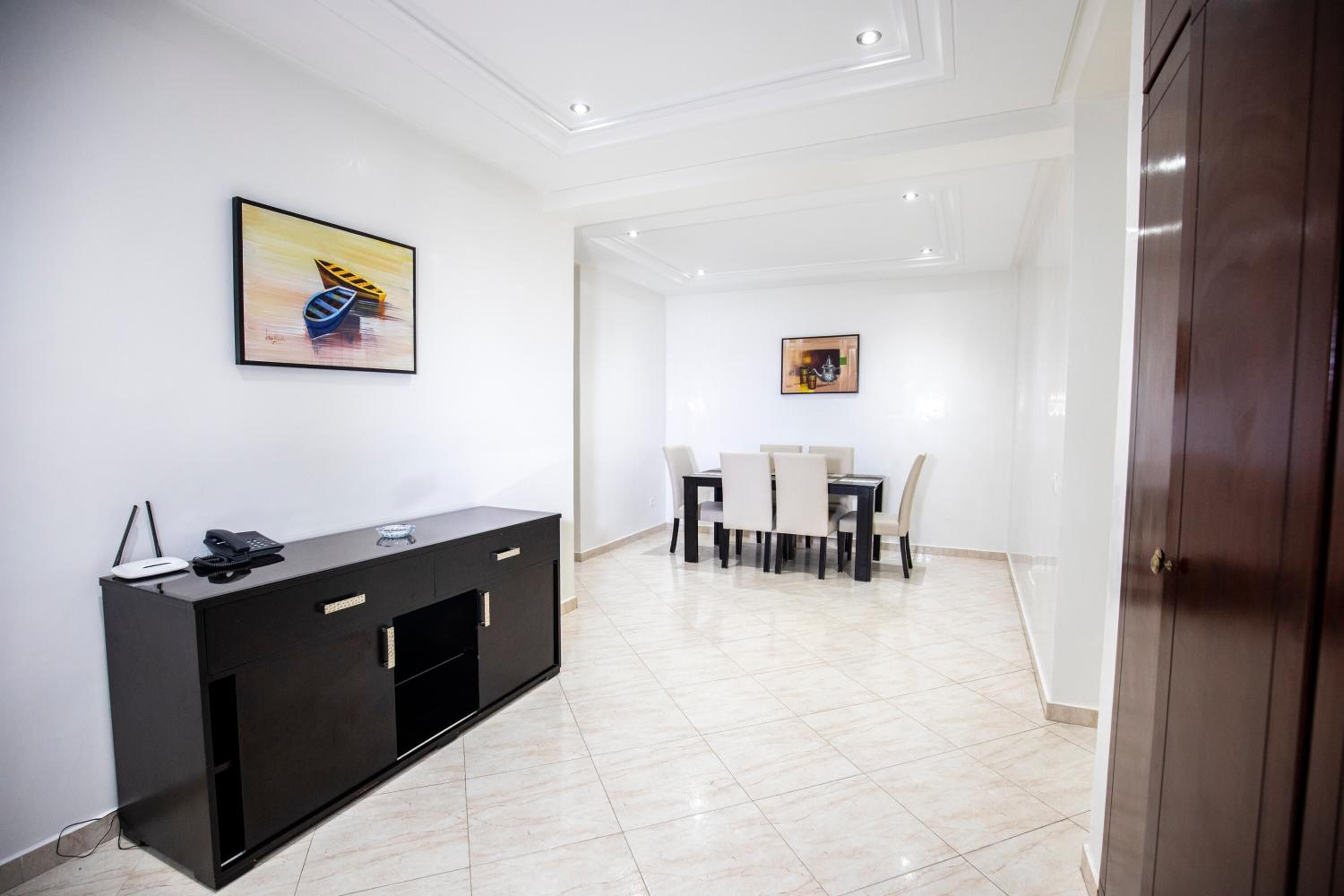 A modern living room with a black entertainment unit, a dining area with a table and chairs, and a hallway leading to a door.