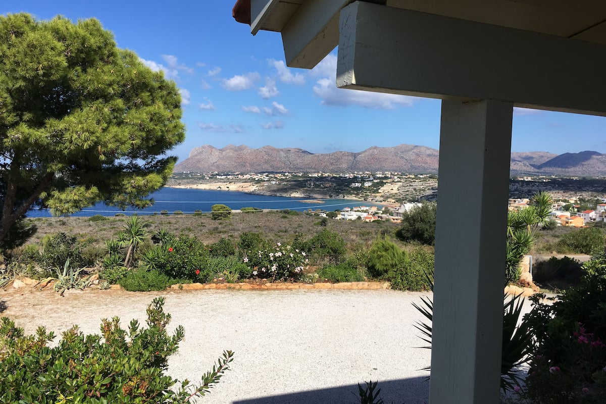 A view from a covered outdoor area overlooking a coastal town with mountains in the background.