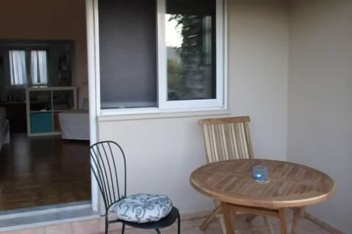 A patio area with a round wooden table and two chairs, one with a patterned cushion.