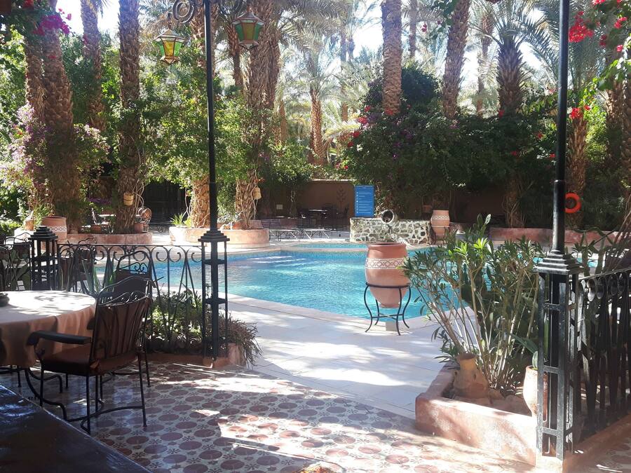 Zona junto a la piscina con un patio empedrado, mobiliario exterior y un muro de piedra.