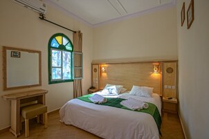 Un dormitorio ordenado con cama, mesitas de noche, un banco, un espejo y una ventana con cortinas.