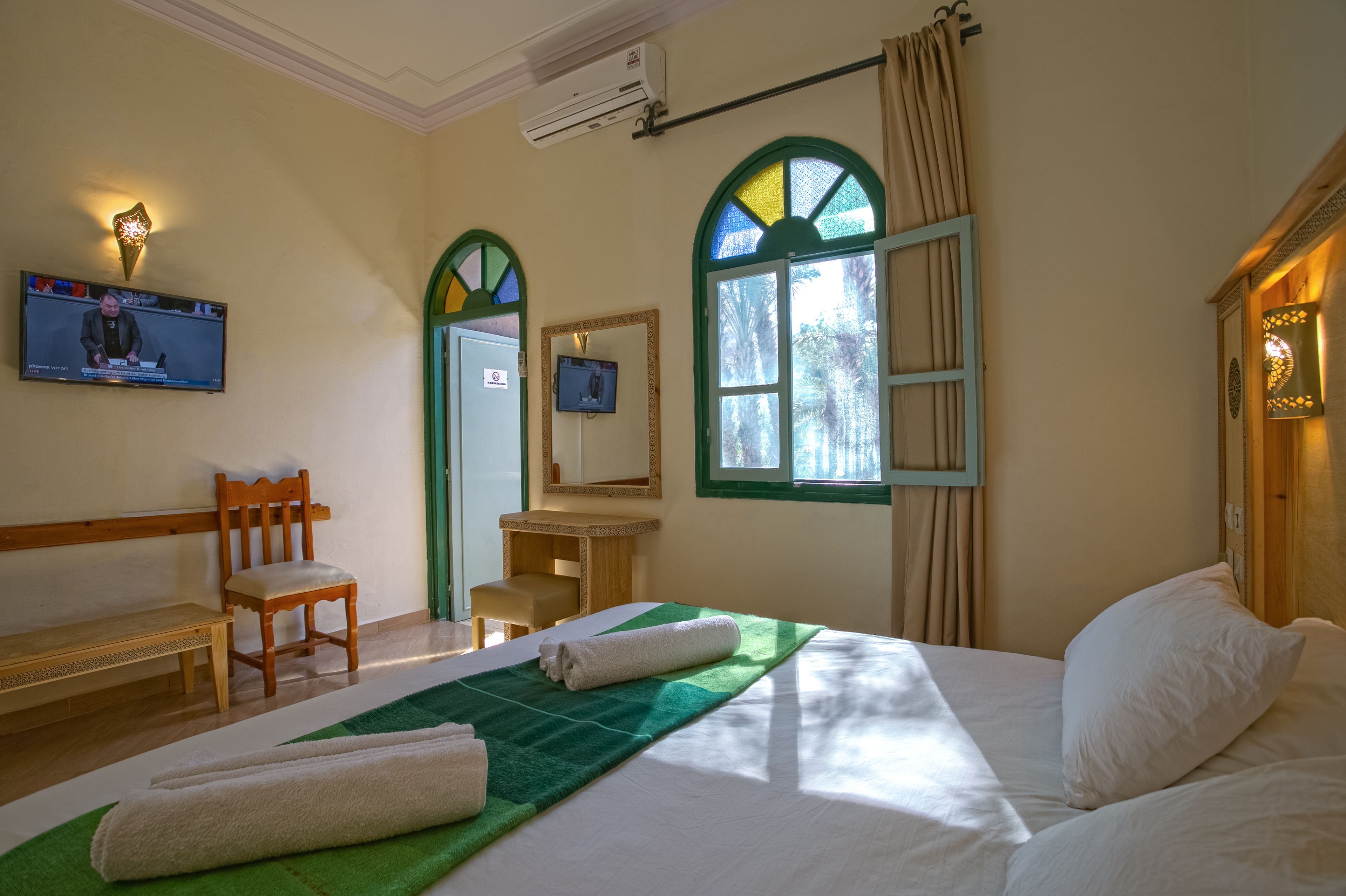 Una habitación de hotel con una cama, una silla de madera, un escritorio, un televisor y una ventana con cortinas.