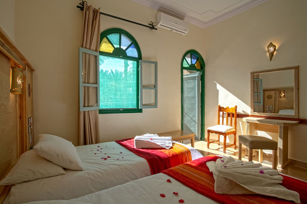 Habitación de hotel con dos camas, un escritorio, una silla y un espejo grande.