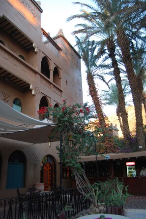Un patio con palmeras, un edificio con arcos y mobiliario exterior.