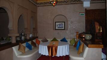 Una zona de estar acogedora con bancos acolchados, una mesa con mantel y una pared decorativa con un cuadro enmarcado.