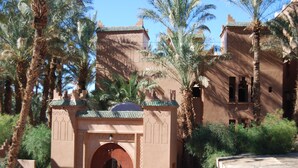 A traditional building with a central arched entrance, surrounded by palm trees and featuring a tiled roof. - Kasbah Sirocco (Zagora)